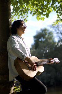 Junger Mann lehnt an einem Baum und spielt Gitarre